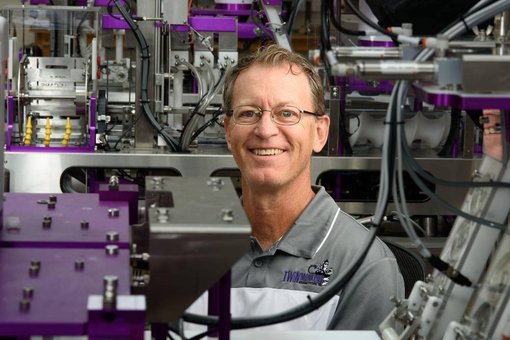 man in glasses standing behind a beer canning machine